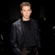 Will Poulter stands in a dark suit against a dark background at a red-carpet event.